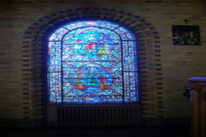Ein Innenblick in eine Kirche mit einem heiligen Kreuzsymbol an der Wand, Buntglasfenstern und einem hölzernen Objekt auf der rechten Seite.