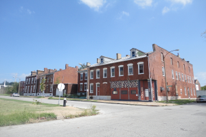 Ein Gebäude mit Polen und Straßenlaternen, umgeben von Bäumen und Fahrzeugen auf beiden Seiten, mit einem Weg, Gras und einem Feuerlöscher unten und Himmel oben.