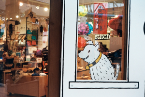 Eine Illustration eines Hundes mit Text auf der rechten Seite und links ein Raum mit Lampen, Flaggen, Regalen, Sofas, Kleidung, Dekorationen, Menschen, Stühlen und diversen anderen Gegenständen.