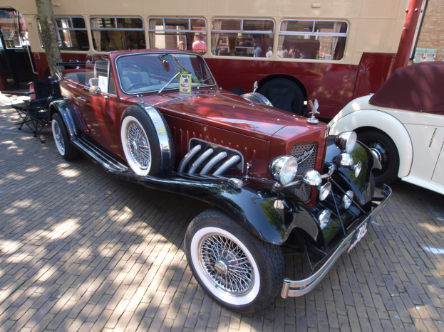 Ein Vintage-Auto neben einem Doppeldeckerbus auf einer Kopfsteinpflasterstraße geparkt, mit Stühlen und einem Baum im Vordergrund, einem Gebäude mit Fenstern im Hintergrund und Menschen im Bus zu sehen.