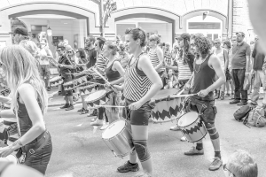 Eine Gruppe von Menschen, die Musikinstrumente auf der Straße spielen, vor einer geschlossenen Glastür mit einem Licht im Hintergrund.