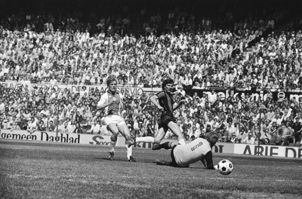 Schwarzes und weißes Foto von Männern, die auf einem Feld Fussball spielen, mit Zuschauern im Hintergrund und einer Bundesliga 1978-79 Ajax 1-1 Hannover 96 Fahne.
