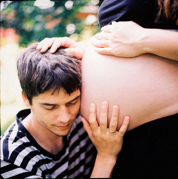 Ein Mann und eine Frau stehen nebeneinander, der Mann berührt zärtlich den Bauch der Frau, mit einem unscharfen Hintergrund, der das Paar und ihr ungeborenes Kind hervorhebt.