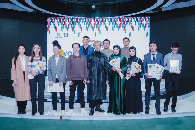 Gruppe von Menschen auf einer Bühne mit Blumensträuseln und Urkunden, mit einem "Jugend-Solar-Awards 2019"-Plakat im Hintergrund.
