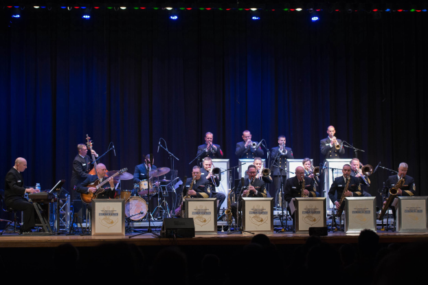 Eine Gruppe Musiker performs auf einer hell erleuchteten Bühne mit "The New Orleans Jazz Band"-Text auf Schildern, während das Publikum darunter zusieht.