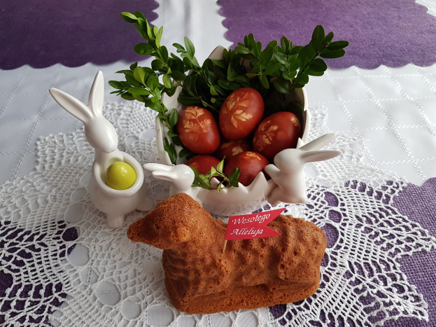 Ein mit einer Decke drapierter Tisch trägt eine Schüssel voller bunter Ostereier mit Osterhasenfiguren darauf.