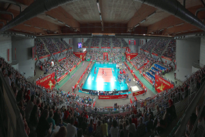 Eine große Halle mit Zuschauern bei einem Volleyballspiel, mit Bannern, Bildschirmen, Deckenbeleuchtung und Geländern unten.