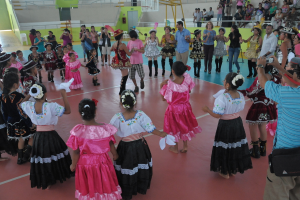 Eine Gruppe von Kindern in Kostümen, mit einem Mädchen und einem Jungen, die in der Mitte tanzen, während andere von oben rechts zusehen.