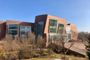 Großes Gebäude mit vielen Fenstern, umgeben von Bäumen, Bänken, Gras und einem Laternenmast, vor anderen Gebäuden und einem klaren blauen Himmel, als der neue Campus der University of Illinois at Chicago identifiziert.