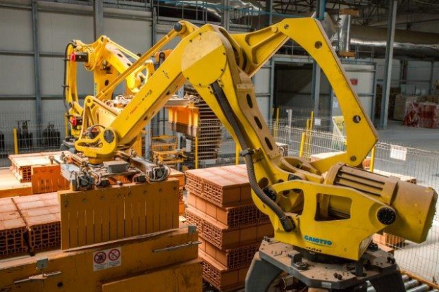 Großes industrielles Lagerhaus mit gestapelten Kisten, Überhead-Kränen, Zaun, Pfählen und einer fernen Wand in einer automatisierten Fertigungsumgebung.