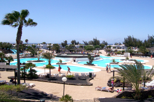 Ein Resort mit von Bäumen umgebenen Pools, Menschen, die zwischen den Pools gehen, Gebäuden im Hintergrund und einem klaren Himmel darüber.