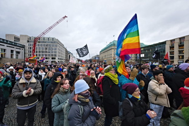 Große Gruppe von Menschen mit LGBTQ+-Rechten-Schildern vor einem Gebäude mit einem Kran im Hintergrund