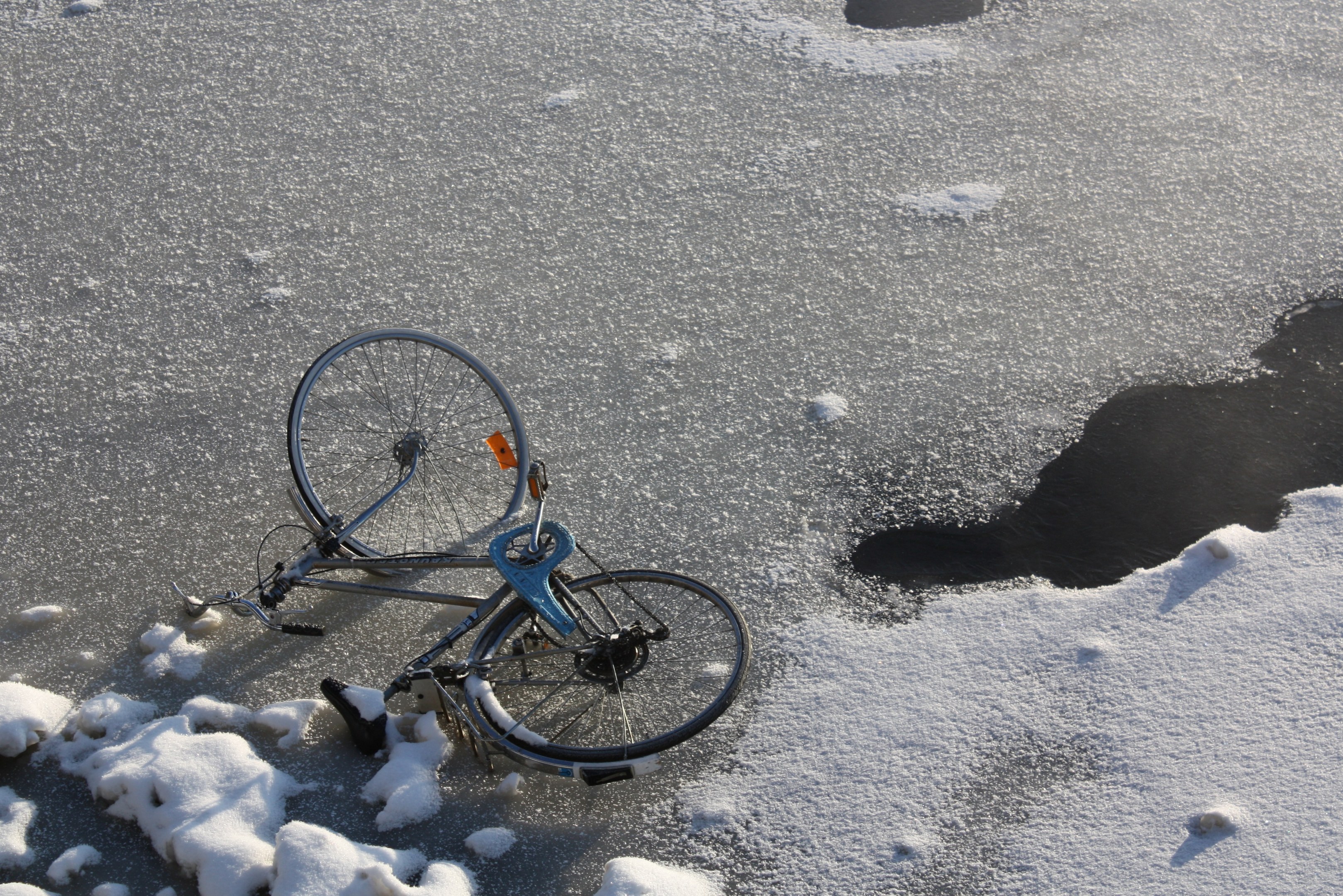 Ein Fahrrad liegt im Schnee neben einer Wasserlache, mit Schnee bedecktem Boden und Fahrrad.