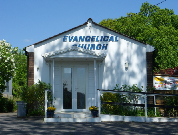Evangelische Kirche mit Straße davor, umgeben von Grünfläche unter einem klaren blauen Himmel.