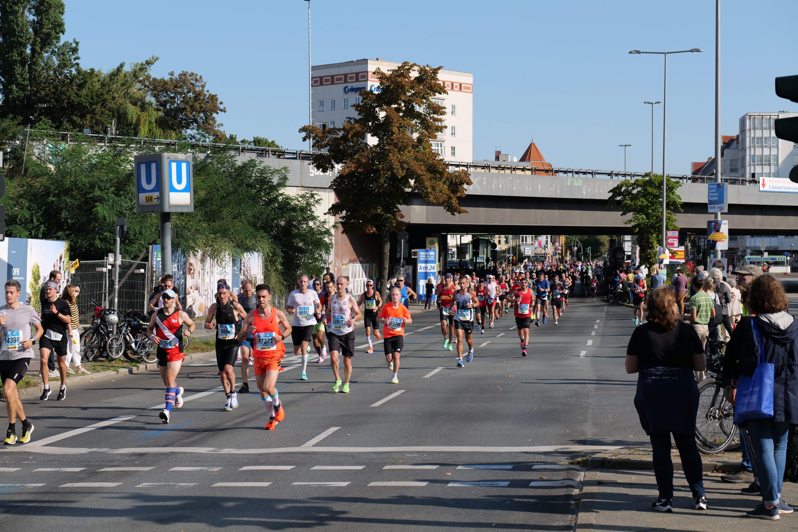 Gruppe von Menschen, die einen Marathon auf einer von Bäumen gesäumten Straße unter einem klaren blauen Himmel laufen.