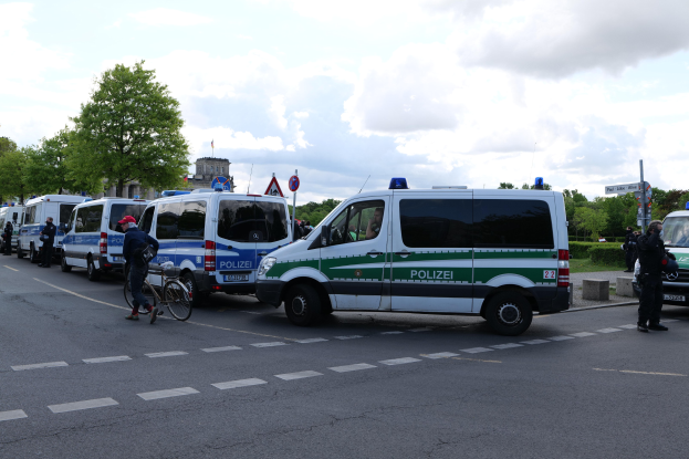 Eine Gruppe von Polizeiwagen, die entlang einer Straße geparkt sind, mit einem Radfahrer im Vordergrund und Gebäuden, Bäumen und Schildern im Hintergrund.