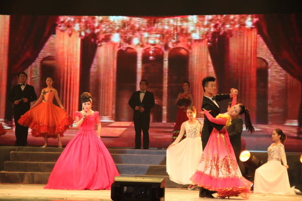 Eine Gruppe von Menschen auf einer Bühne mit Lichtern, Stufen und einem Hintergrundbild, mit einem Lautsprecher unten, was eine Tanzvorstellung vermuten lässt.