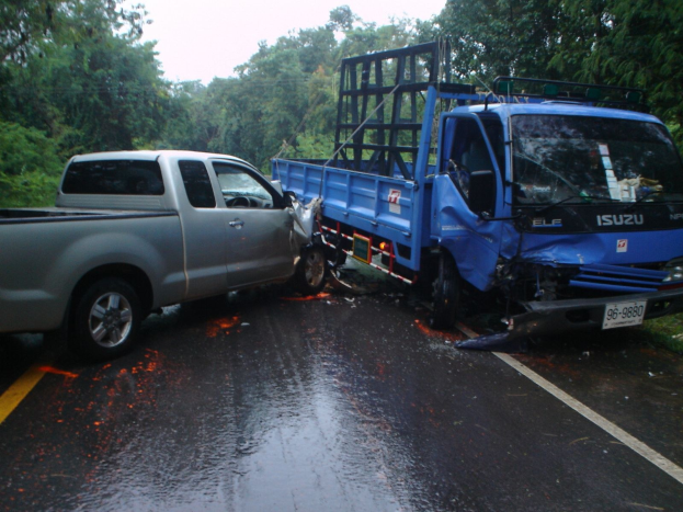 Ein beschädigtter Lkw mit eingedrücckter Front und verbeulter Karosserie am Seitenstreifen einer Straüe, umgeben von Bäumen unter einem klaren blauen Himmel.