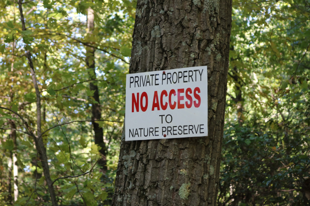 Ein Baum mit einem "Privatgrundstück Kein Zugang zum Naturreservat" Schild auf seinem Stamm, umgeben von dichtem Wald im Hintergrund.