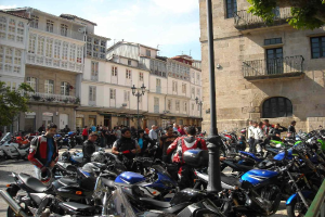 Ein cremefarbenes Gebäude mit zahlreichen Fenstern, das an ein Backsteingebäude mit einer Metallbalustrade angrenzt, mit mehreren geparkten Fahrrädern und Menschen, die sich vor dem Gebäude unterhalten.