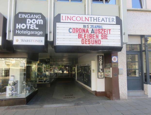 Außenansicht des Lincoln Theaters in Berlin, Deutschland, mit Glasfenstern und -türen, einem Schild mit Text und einem durch die Fenster sichtbaren Innenraum, der eine belebte Stadtkulisse suggeriert.