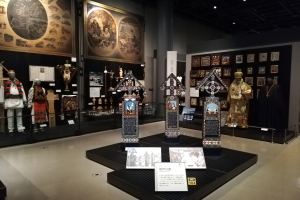 Ein Museumsraum mit verschiedenen Gegenständen, darunter Schaufensterpuppen in Kostümen, Fotorahmen an den Wänden, eine Säule und Deckenleuchten, gewidmet der Geschichte Japans.