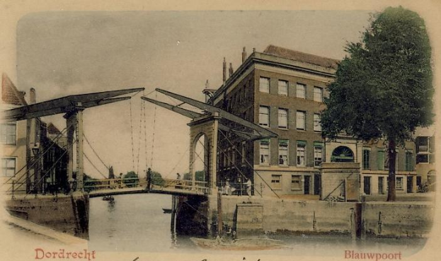 Altes Schwarz-Weiß-Foto einer Brücke unter Bau, die einen Fluss überspannt, mit Gebäuden, Bäumen und einem klaren Himmel im Hintergrund und verstreuten Baumaschinen und Materialien am Boden.