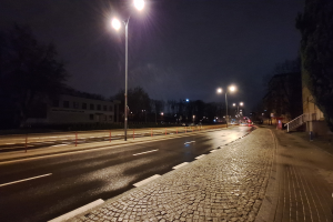 Eine nächtliche StraßenSzene mit Straßenlaternen, die die Straße, Gehwege, Geländer, Bäume, Gebäude und andere Gegenstände beleuchten, mit dem Himmel im Hintergrund.