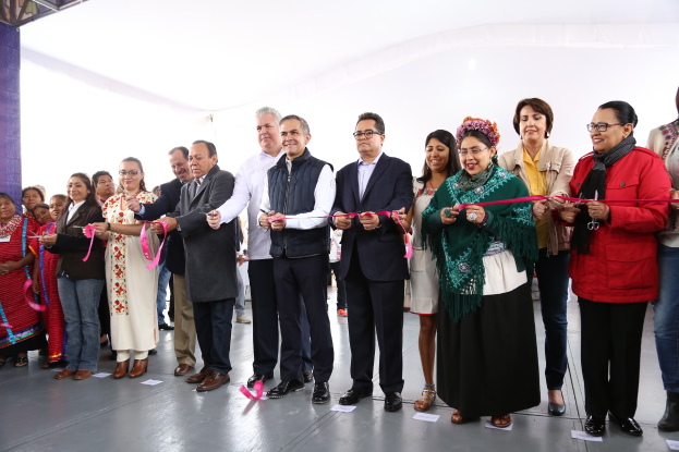 Eine Gruppe von Menschen bei einer Eröffnungszeremonie, die strahlen und eine Schere halten, mit Papieren auf dem Boden und einem weißen Tuch im Hintergrund.