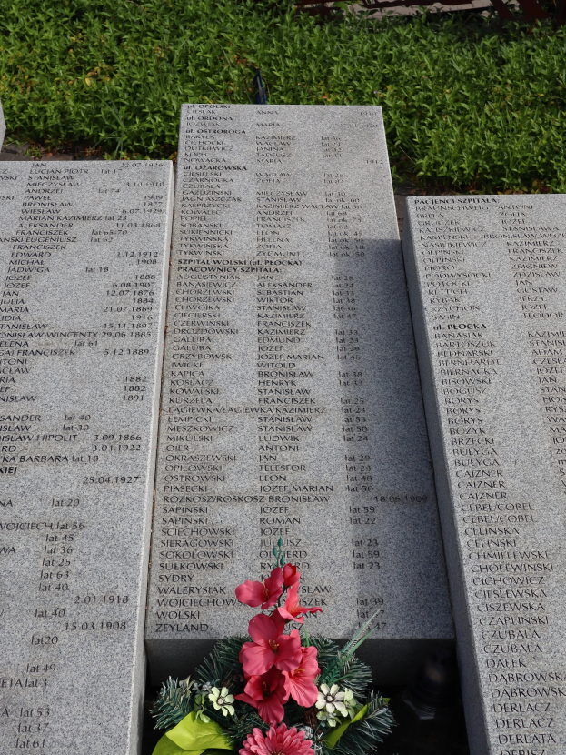 Ein Gedenkstein mit einem Blumenstrauß darauf, umgeben von grünem Gras.