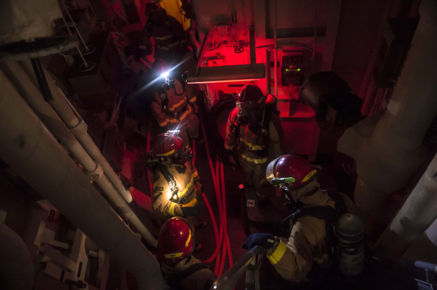 Feuerwehrleute in Helmen und Sauerstoffflaschen stehen in einem dunklen Raum mit Rohren auf beiden Seiten und bereiten sich auf eine Rettungsoperation in der Nähe von Maschinen und anderen Gegenständen vor.