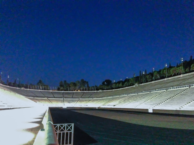 Olympiastadion bei Nacht, beleuchtet von Stadionlampen und Sternen, umgeben von Bäumen und Pfählen, mit Boden unten.