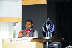 Ein Mann steht neben einem Rednerpult und spricht mit einer Wand im Hintergrund.