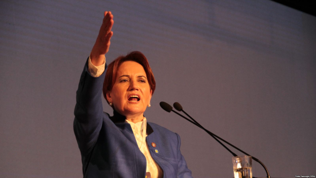 Eine Frau steht an einem Rednerpult mit einem Glas Wasser und zwei Mikrofonen und hält eine Rede vor einem Bildschirm, wahrscheinlich zu einer Regierungsentscheidung, Frauenrechte zu verbieten.