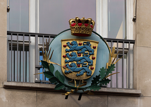 Wappen der britischen Königsfamilie auf der Fassade eines Gebäudes mit einer Krone und einem Logo aus Blättern im Hintergrund.