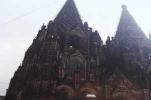 Der Kölner Dom in Köln, Deutschland, mit seinen Türmen, die in den Himmel ragen, und einigen Menschen, die vor dem Gebäude mit sichtbaren Kabeln im Hintergrund stehen.
