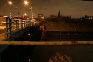 Eine Brücke überspannt einen Fluss mit zahlreichen Straßenlaternen und im Hintergrund sind Gebäude zu sehen.