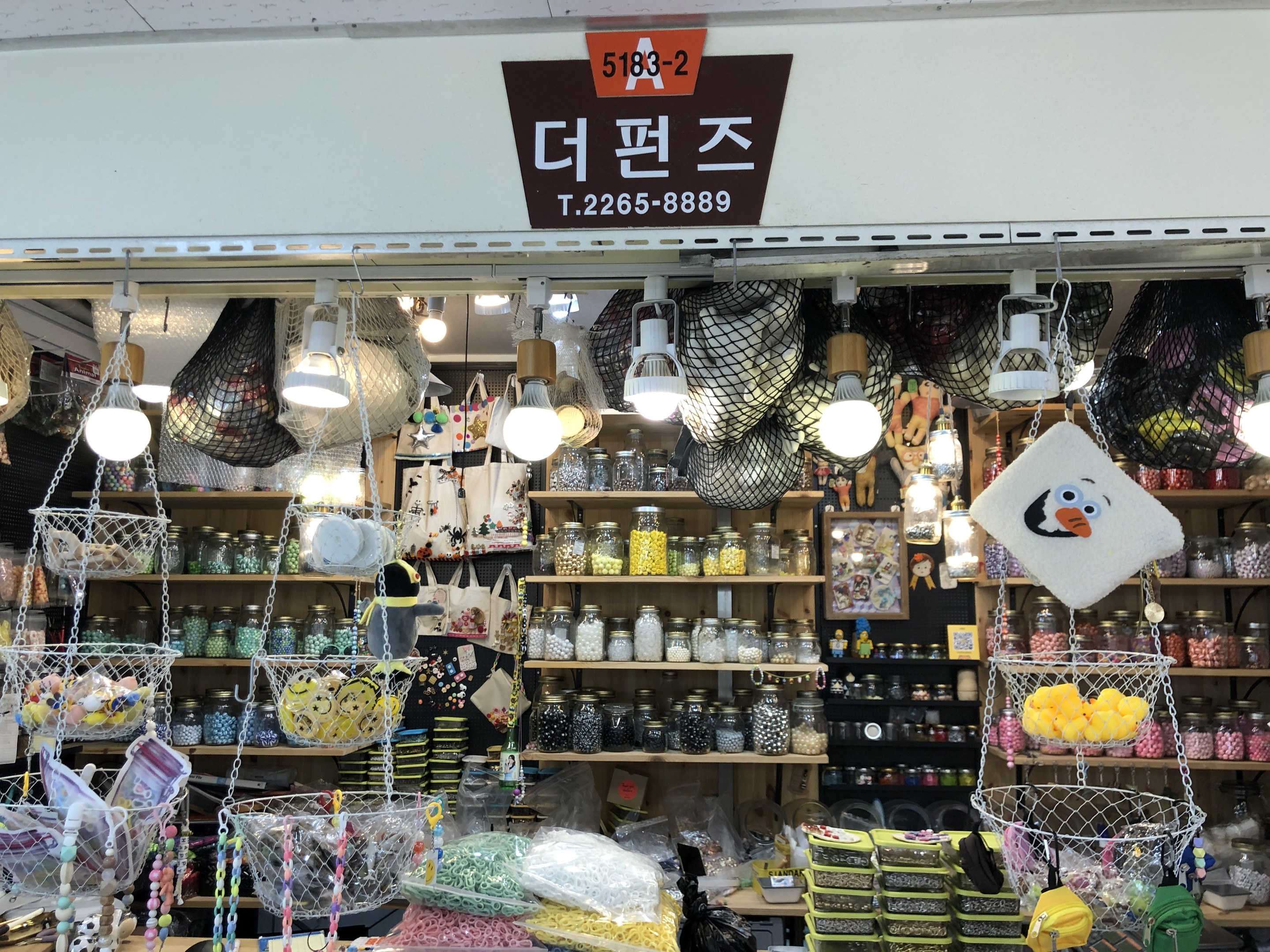 Ein unordentlicher Laden in Seoul mit verschiedenen Artikeln wie Korbwaren, Lichtern, Flaschen und Spielzeugen auf Regalen, mit einer Tafel oben, die anzeigt, dass es einer der besten koreanischen Shops ist.