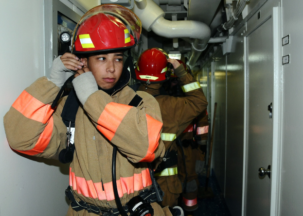 Feuerwehrleute in Uniform, die in einem Raum mit Rohren und Ausrüstung stehen, wahrscheinlich während eines Übungsbetriebs.