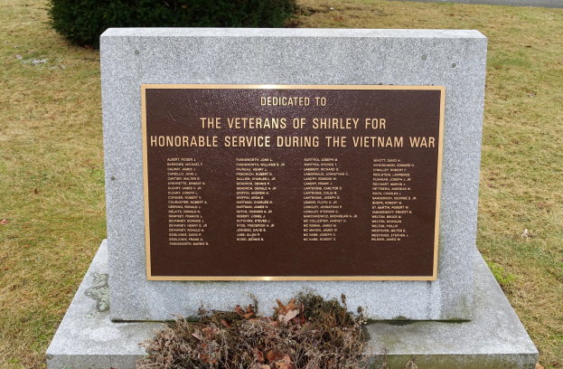 Denkmalstein mit einer Gedenktafel für die Vietnam-Veteranen von Shirley, umgeben von Gras und Pflanzen in der Nähe einer Straße.