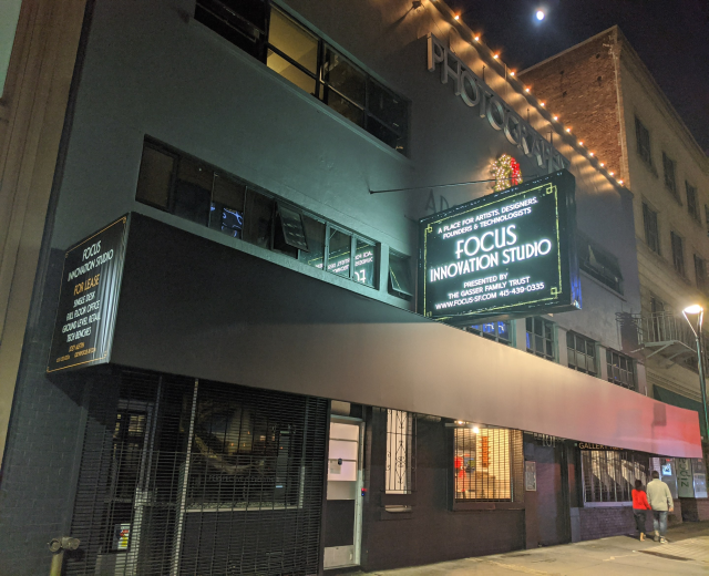 Außenansicht des Focus Innovation Studio in New York City bei Nacht, mit beleuchteten Gebäuden, Menschen auf dem Bürgersteig und sichtbarem Himmel im Hintergrund.