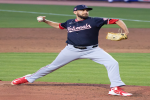 Ein Baseballspieler in einer Mütze und Handschuhen wirft auf einem grünen Feld, mit Menschen und Texttafeln im Hintergrund, die einen World-Series-Sieg der Washington Nationals anzeigen.
