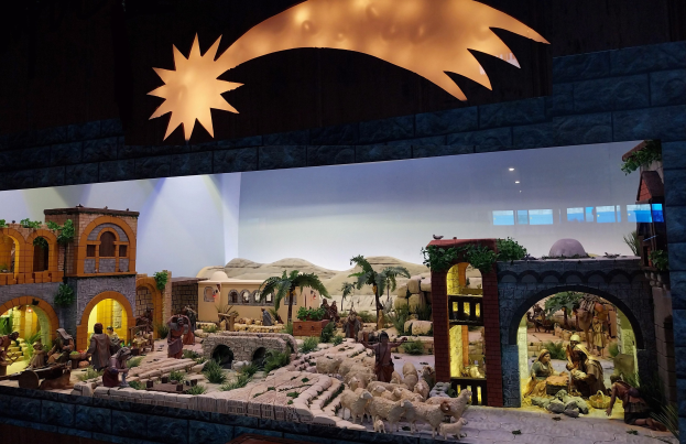 Eine Krippe in einem Museum mit Menschen, Tieren, Häusern, Bäumen und anderen Gegenständen und einer Lampe, die die Szene von oben beleuchtet.