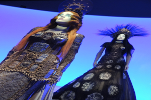 Zwei Schaufensterpuppen in verschiedenen Outfits und Kopfbedeckungen.