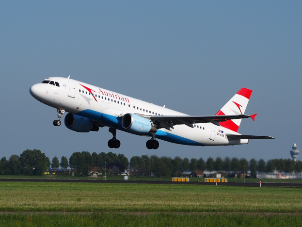 Airbus A320-200 der Austrian Airlines startet vom Frankfurter Flughafen mit grünem Gras, Bäumen, Gebäuden und einem Tower im Hintergrund.