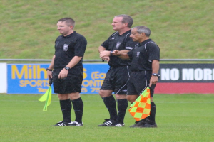 Drei Männer in schwarzer Kleidung mit Fahnen vor Gras und Bannern.
