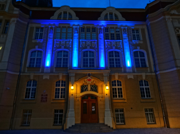 Ein großes Gebäude mit blauen Lichtern, das sich gegen den Nachthimmel abhebt, mit Fenstern, einer Tür und umgebenden Lampen.