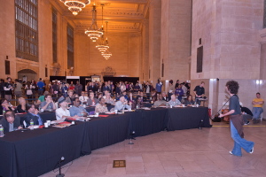 Eine Konzertszene mit einer Menge Menschen, ein Mann, der auf der rechten Seite Gitarre spielt und singt, eine Wand und Fenster im Hintergrund, Lichter oben und ein Boden unten.
