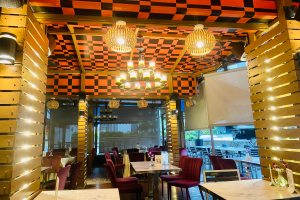 Ein Restaurant-Innenraum mit Tischen und Stühlen unter einer karierten Decke, dekoriert mit Blumenvasen und anderen Gegenständen, während die Wände mit Lichtern und Kronleuchtern geschmückt sind.