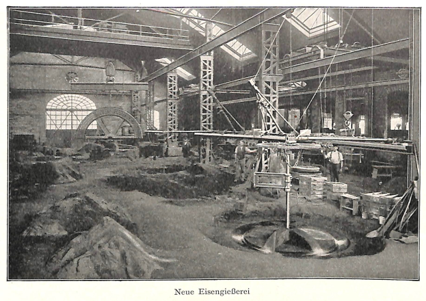 Schwarzes und weißes Foto einer deutschen Fabrik aus dem 19. Jahrhundert mit Arbeitern, die an einer Maschine arbeiten, umgeben von Metallstangen und -pfählen, beschriftet mit "Neue Eisenglebeerei, die erste Fabrik in Deutschland" unten.